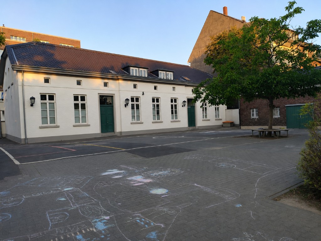 Katholische Grundschule Niederkassel – Schulhof mit Kreidezeichnungen und Schulgebäude in der Abendsonne (Catholic primary school Niederkassel – schoolyard with chalk art and building in evening light)